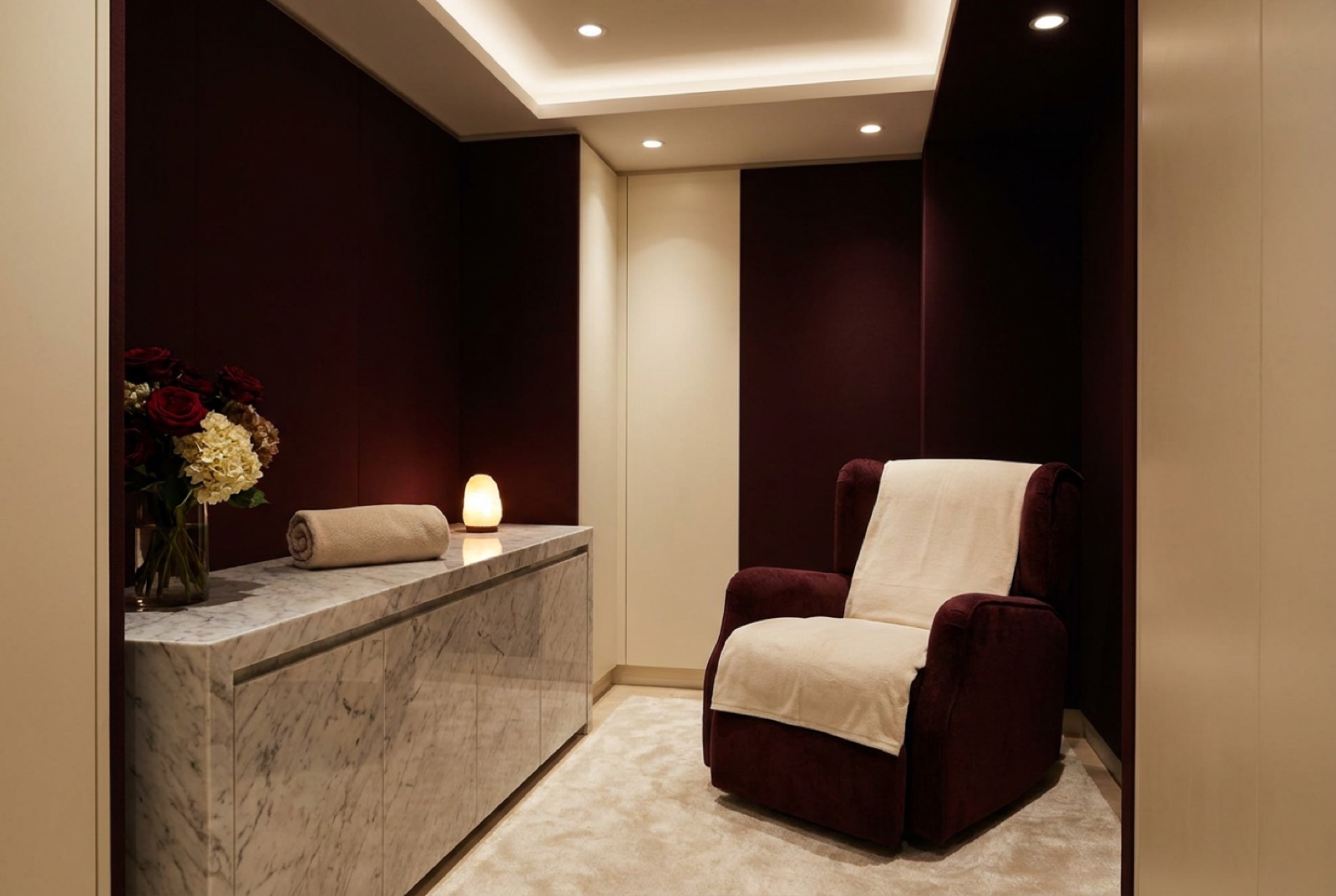 A calm, warmly lit treatment room with claret walls, marble console and fresh flowers