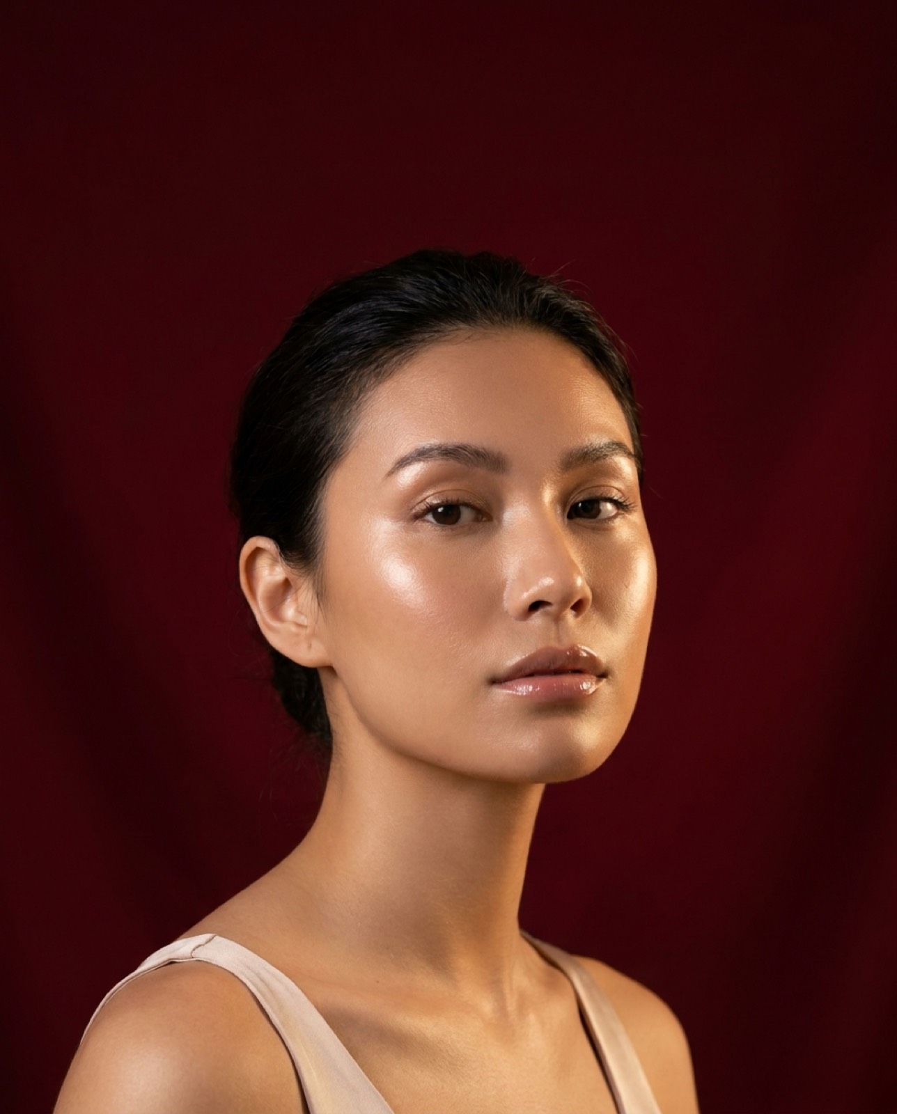 Beauty portrait of a woman with dark hair and luminous, radiant skin against a deep claret background