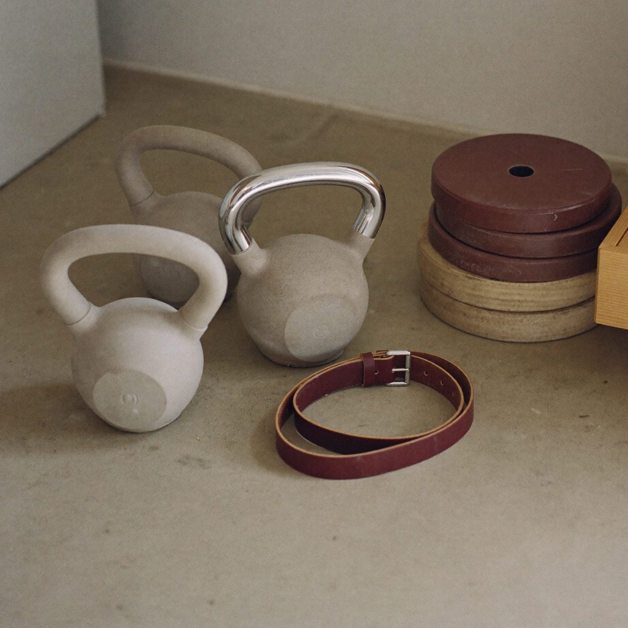 Kettlebells, weight plates and a lifting belt arranged on pale concrete