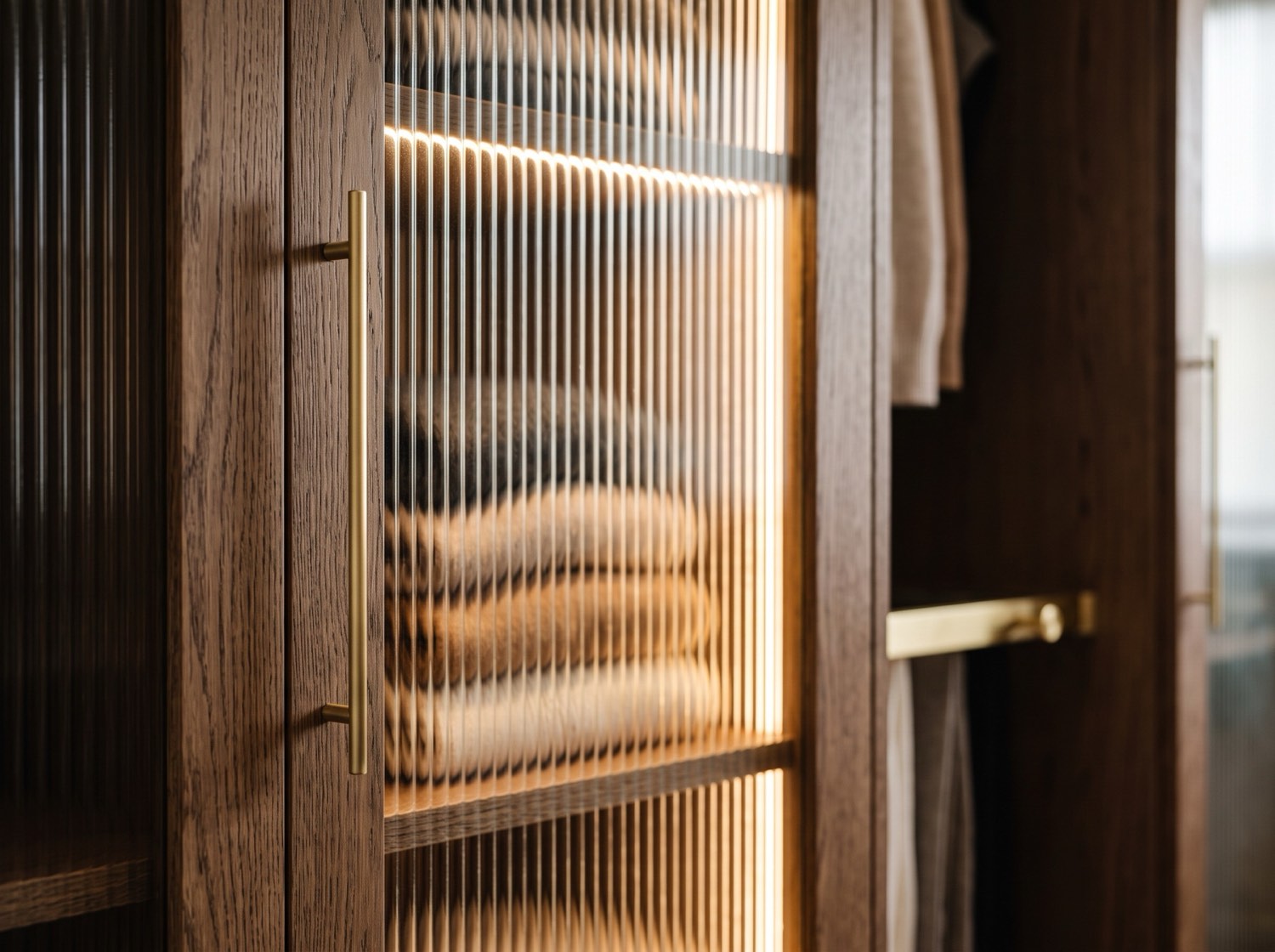 Close-up of a fluted reeded glass wardrobe door with a brushed-brass handle in smoked oak